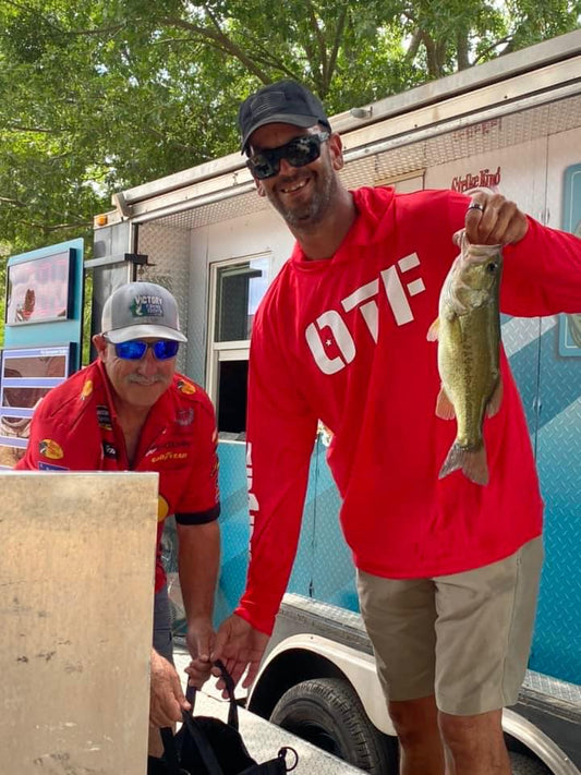 One Tribe Foundation red hooded fishing shirt.  OTF on the front and the OTF logo with shield on back.